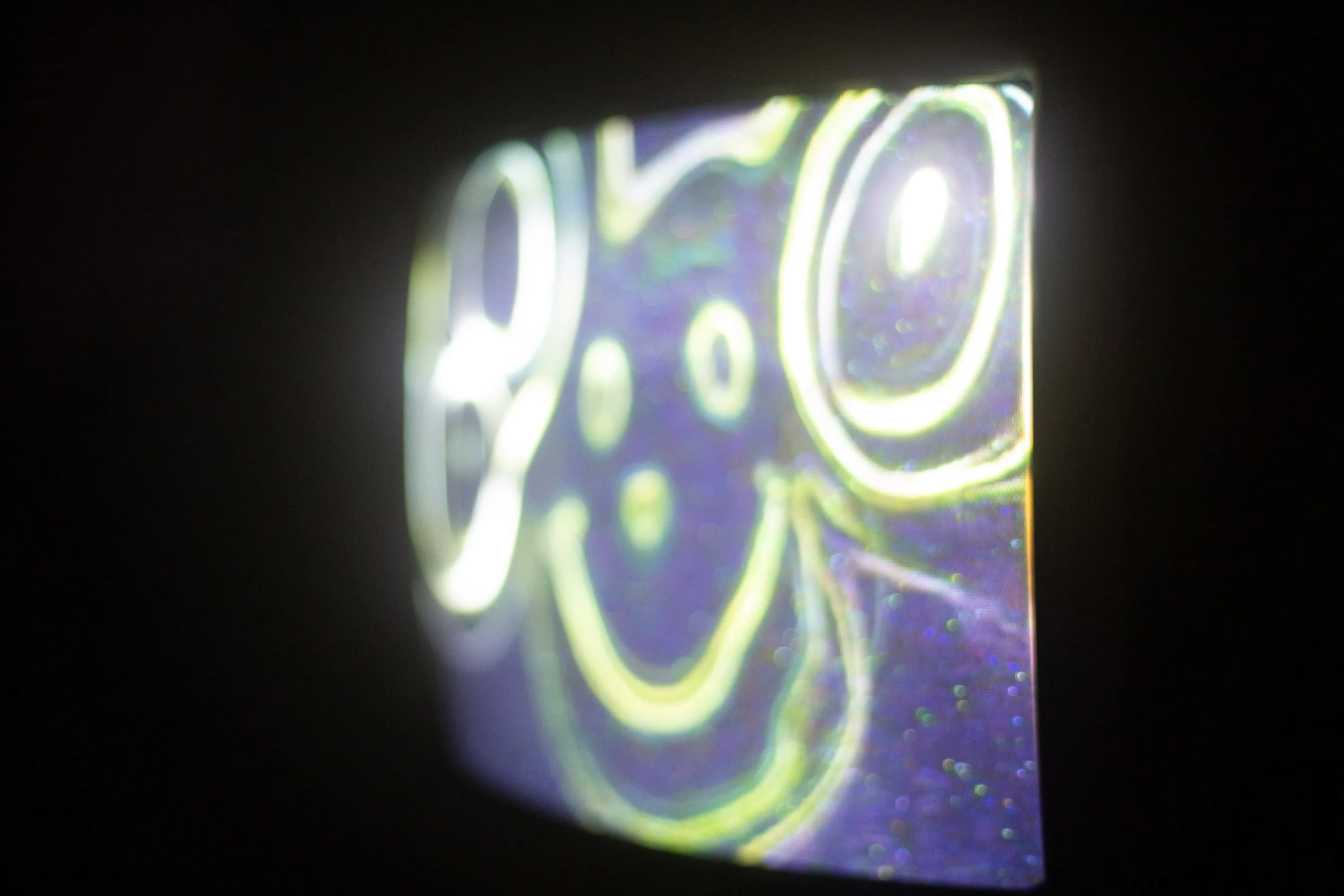 A CRT TV shows yellowy green warped acid smiley slightly burred with edge detection applied