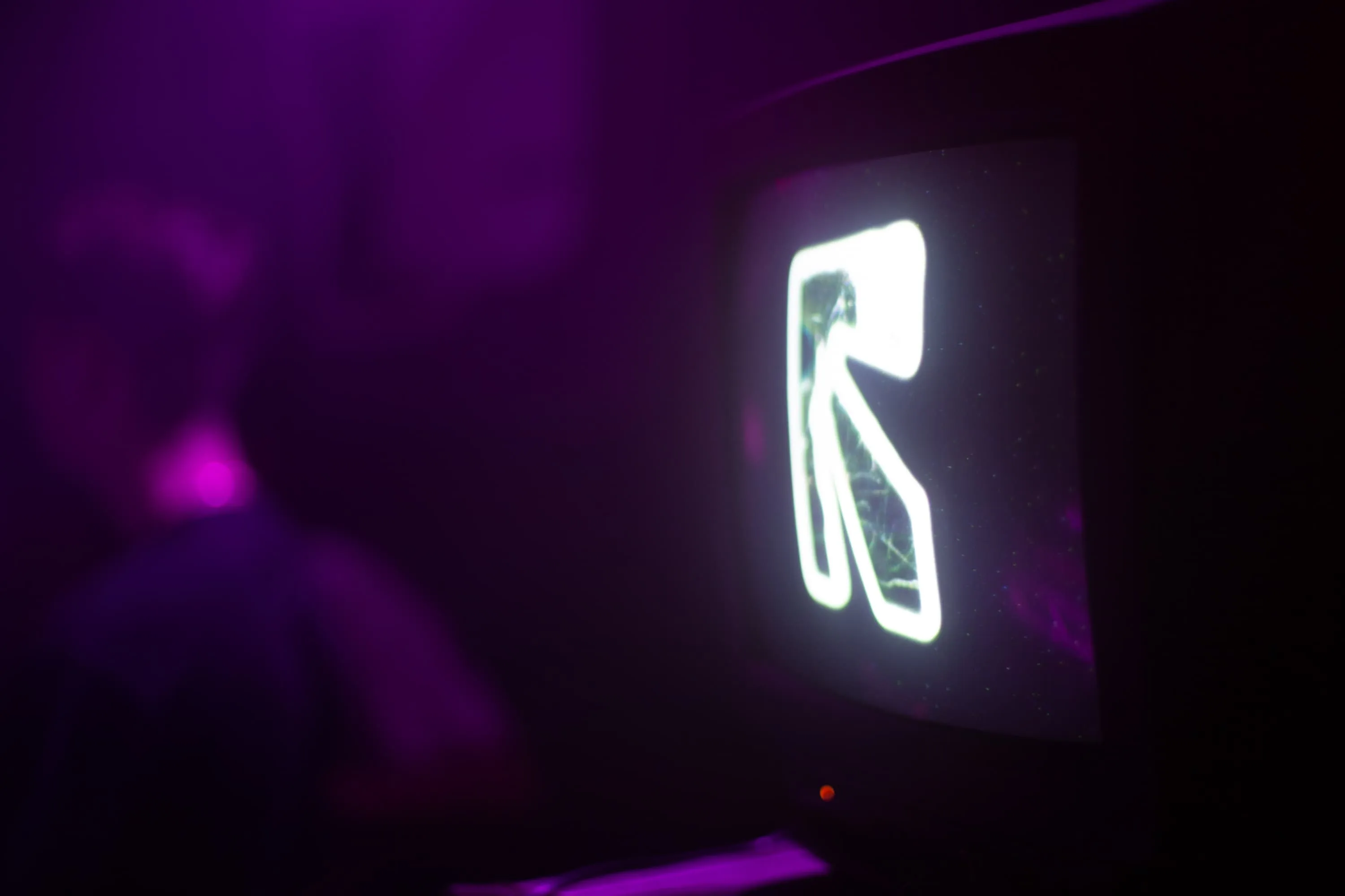 A CRT TV shows green logo in 3d with edge detection applied, a man dances blurred in the background