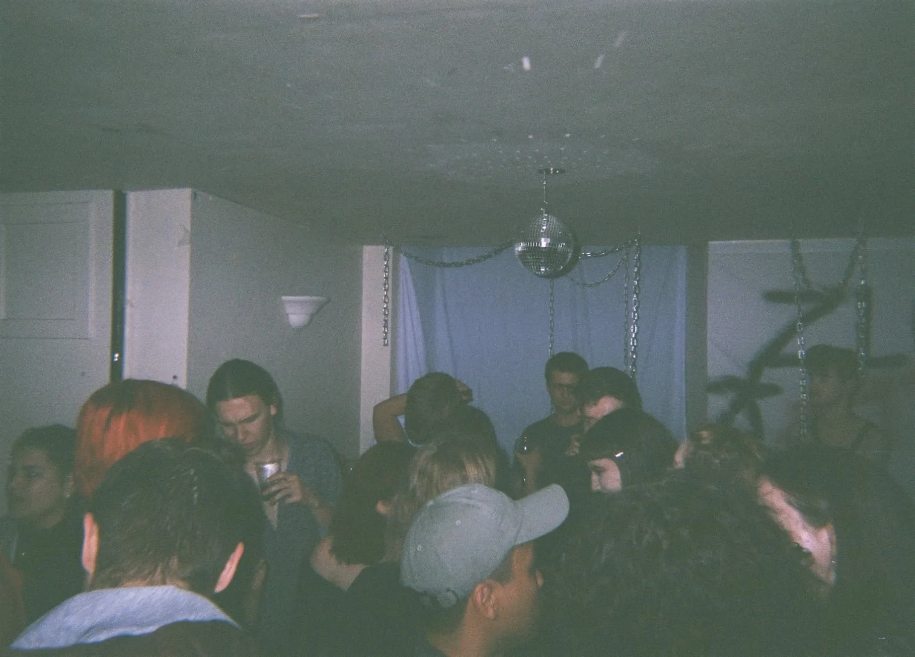 A crowd dance and stand at D2, a small basement space. At the back left there is grafitti with the words Zloto. In the middle of the ceiling there is a disco ball.