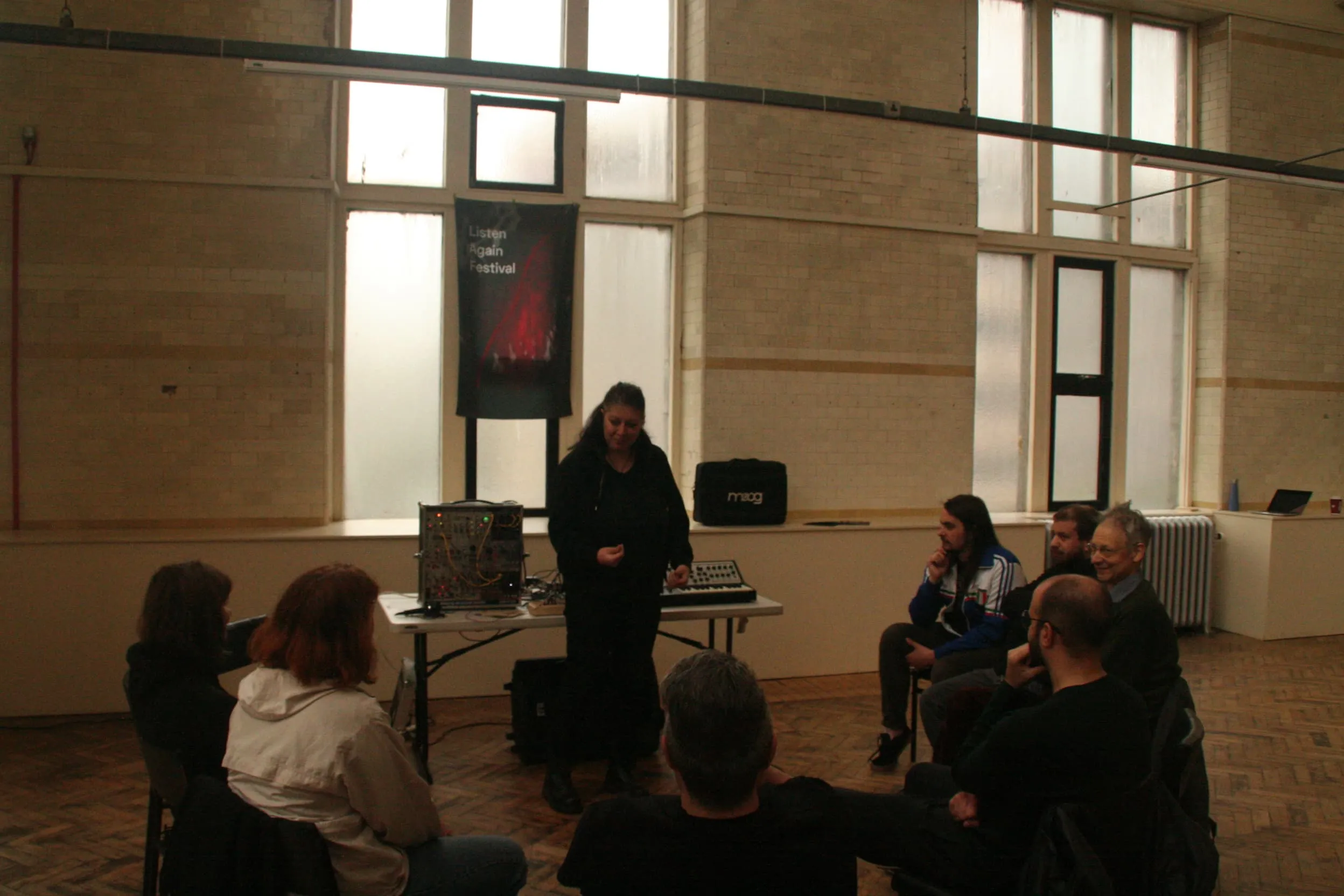 A woman gives a modular synthesis workshops as a small ground are gathered round sitting in a circle.