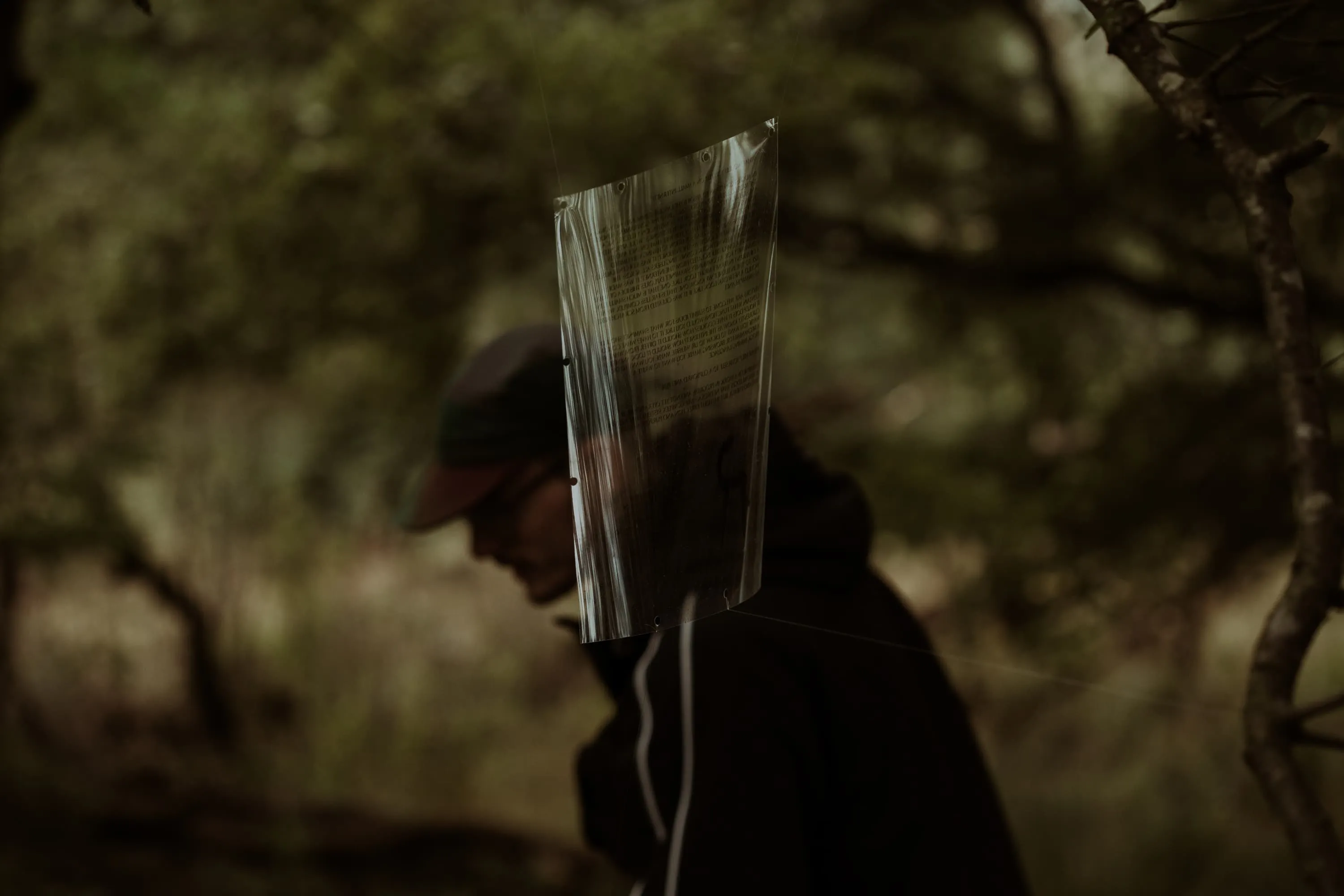 a transparent piece of plastic with small text on it floats in mid-air held by invisible in front of a blurry me wearing a green cap and black jacket
