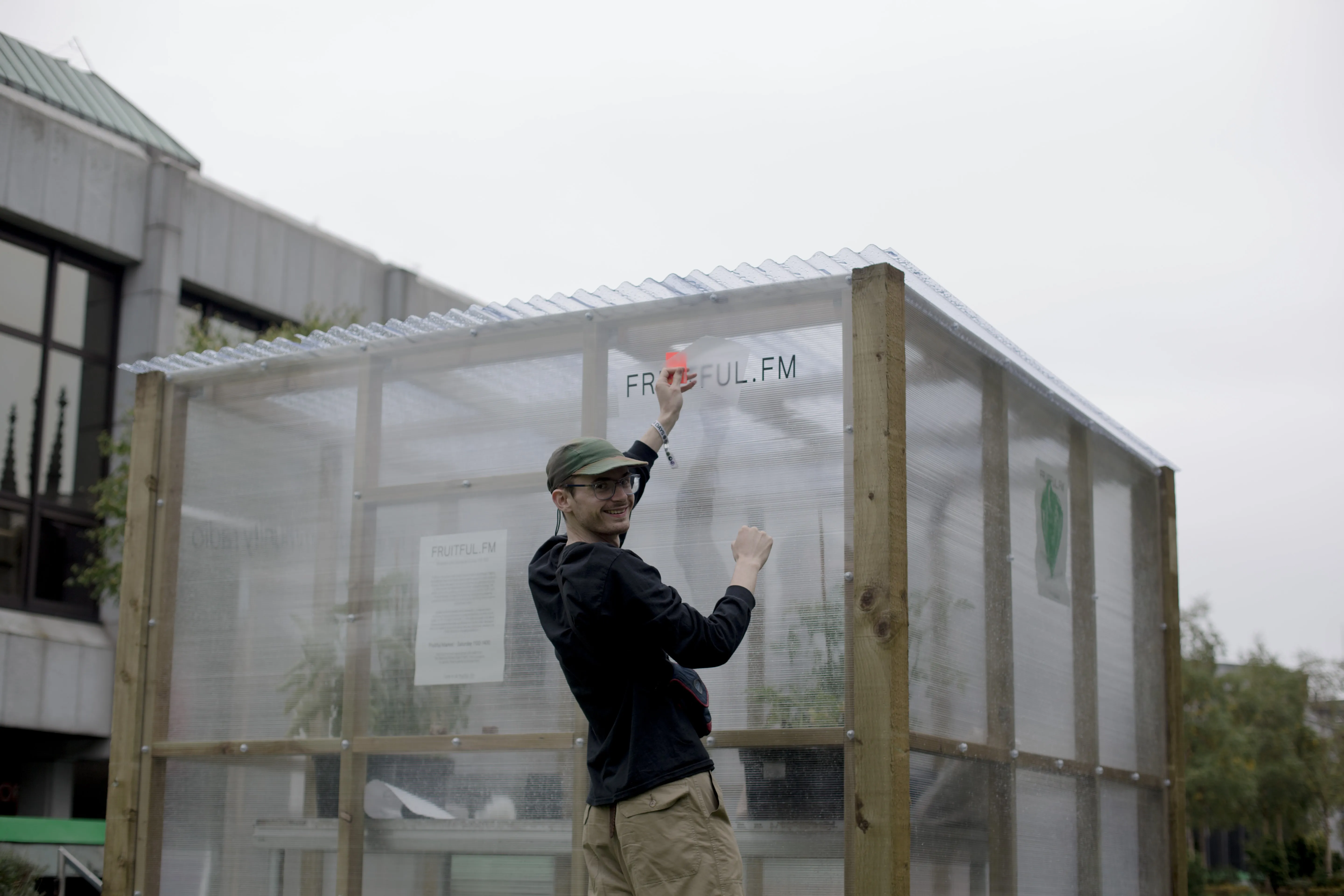 A man smiles as he installs a vinyl onto the front of a greenhouse reading Fruitful.FM