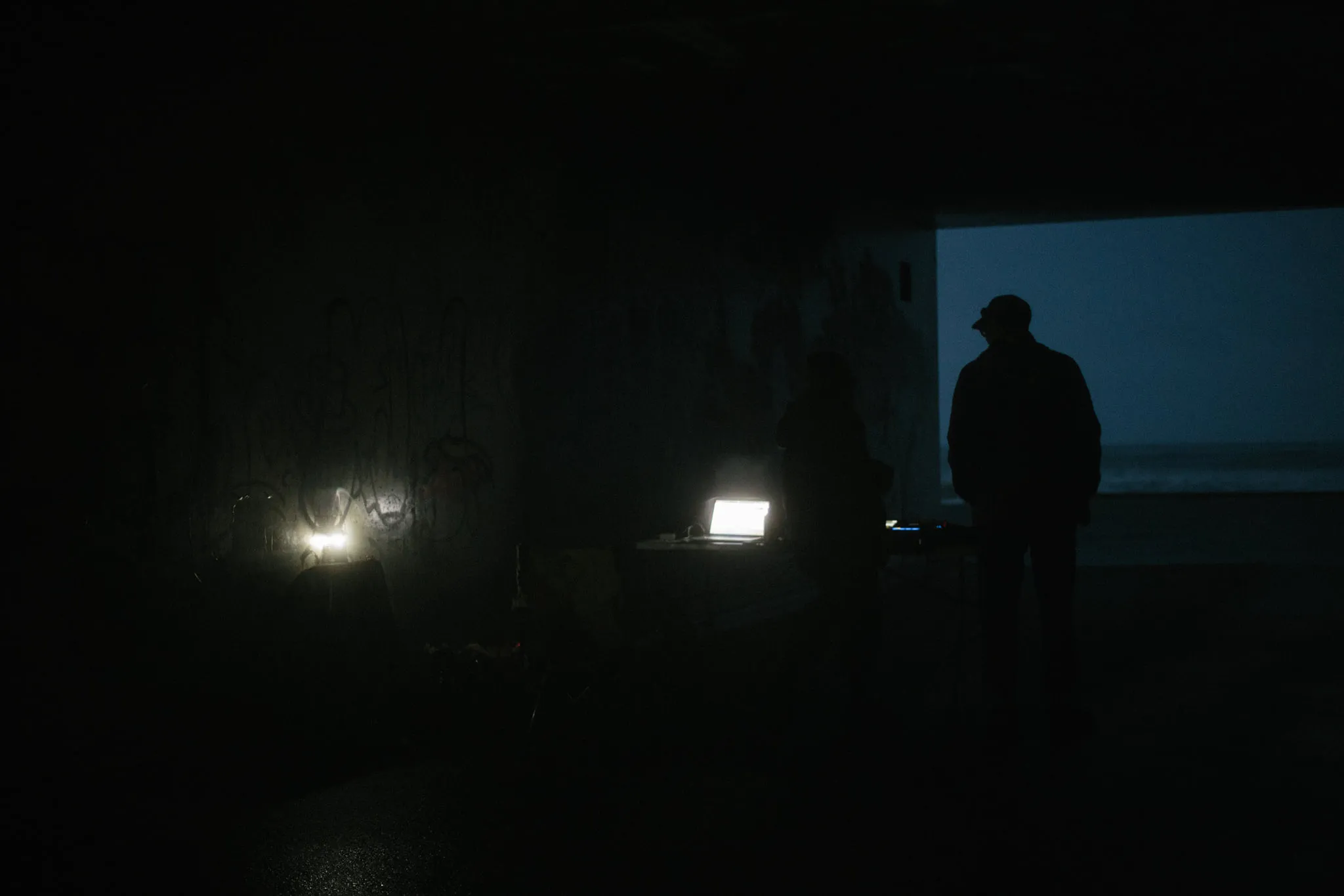 It's dark, its october in Aberdeen, maybe arond 8pm and light from a electric lantern and laptop fill the scene with dim light. Figures can just be made out standing inside a tunnels next to the beach.