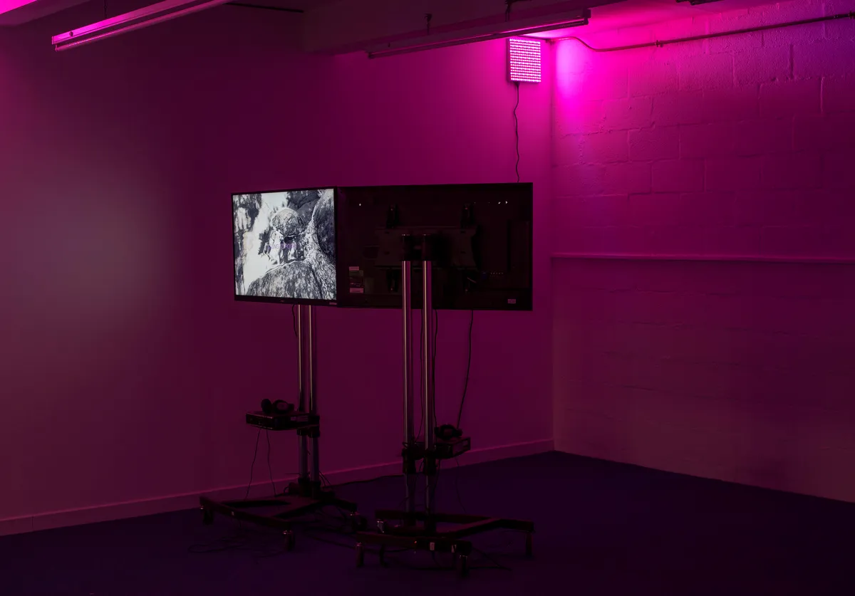 Pink light at the top of the image fills with basement space with a nice pinky glow. Two TVs on stands facing opposite directions are installed in a corner showing Lavendar Heated to 60c film.