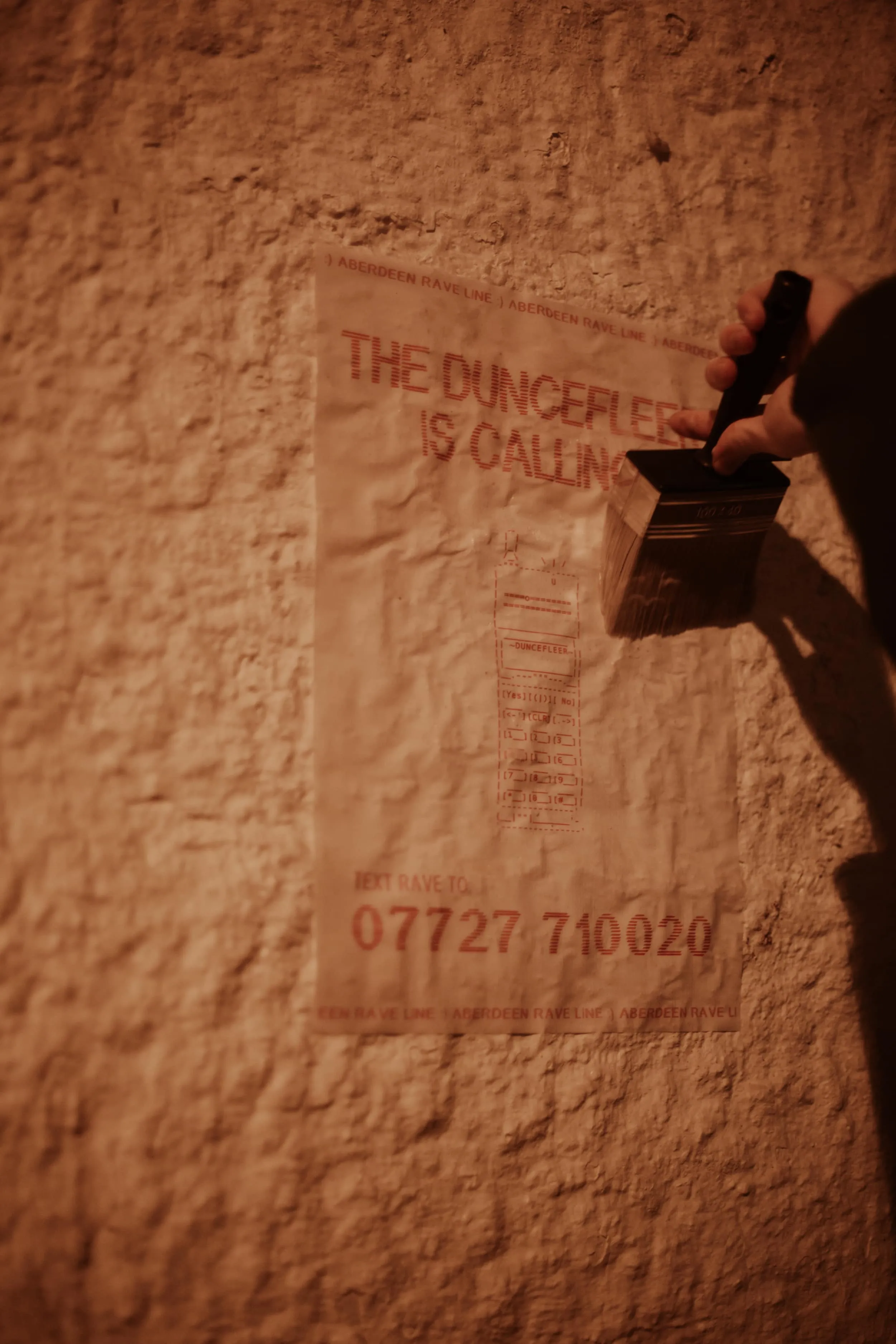 Hand holding large paint brush pasting up poster on white brick wall
